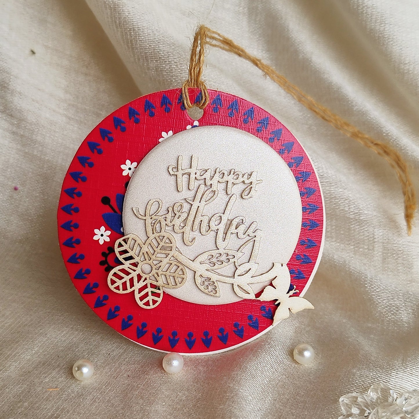 A gift tag with a three-layer design, decorated with laser-cut flowers and butterflies, hanging from a string.