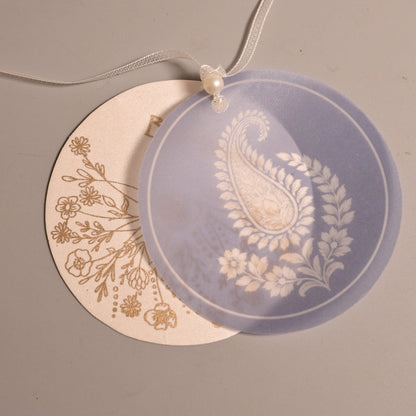 Two round hanging tags on a thin white string, one in translucent lavender with a white paisley and floral design, and one in cream with a gold floral print.
