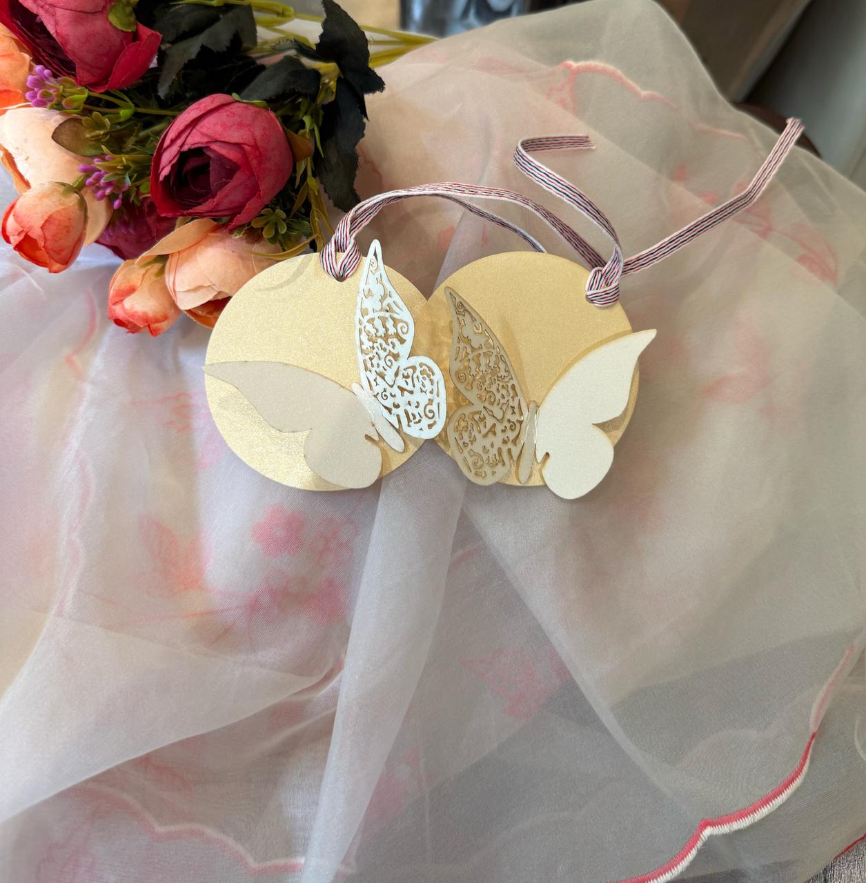 A round off-white metallic paper gift tag with a ribbon handle and laser-cut butterflies design