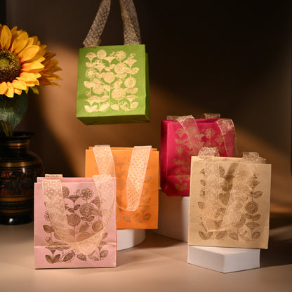 A set of five handmade paper bags in various colors, each featuring a gold floral print and ribbon handles.