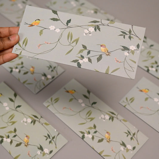envelope featuring a delicate botanical print with small yellow birds, green leaves, and white blossoms on a pale gray background.