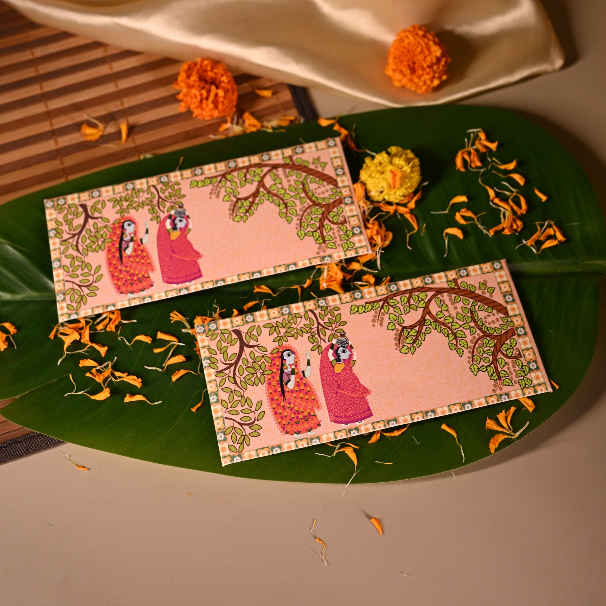 Decorative envelopes with floral designs on a green leaf, with a beige fabric and small flowers in the background