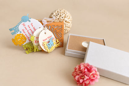 A styled flat-lay of a gift set featuring colorful animal-shaped paper tags with a warm welcome message, an orange laser-cut box insert, a white gift box with its lid off