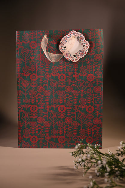 green paper bag with red floral motifs and ribbon handle