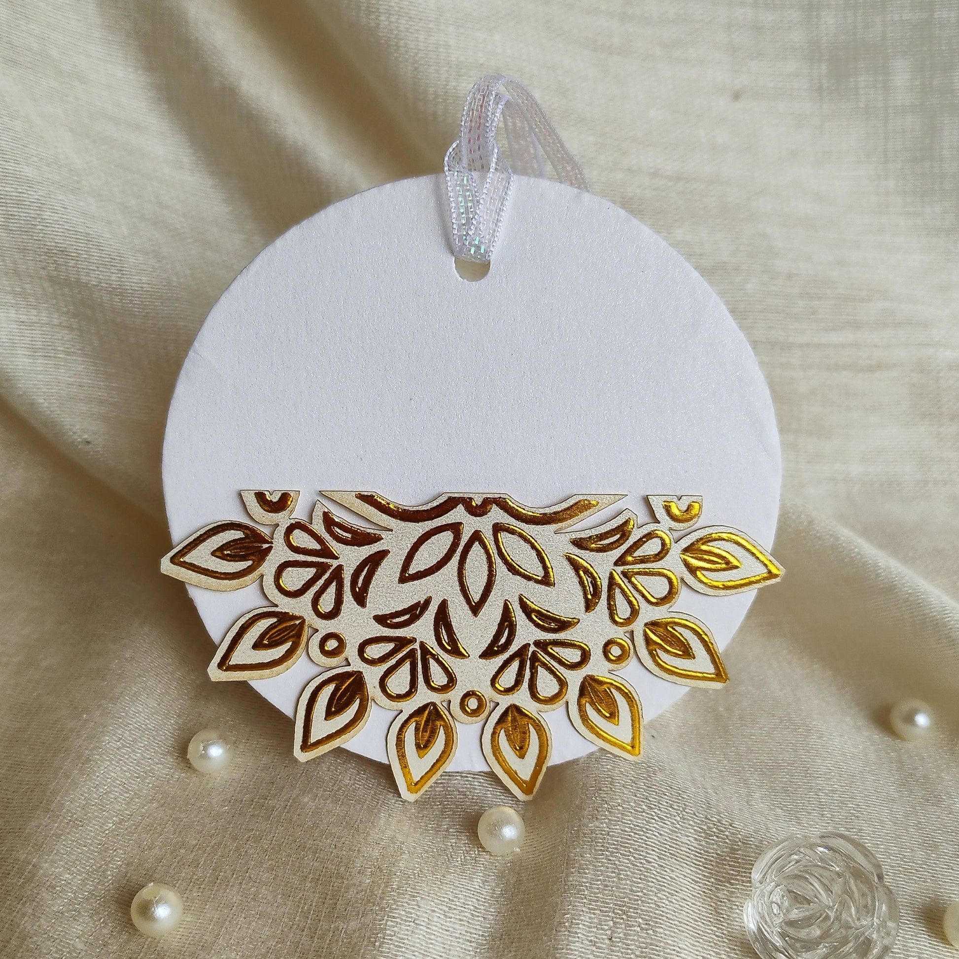 A half round gift tag with a golden foil embossing in a half-sun pattern design, attached to a white circular base with a ribbon.