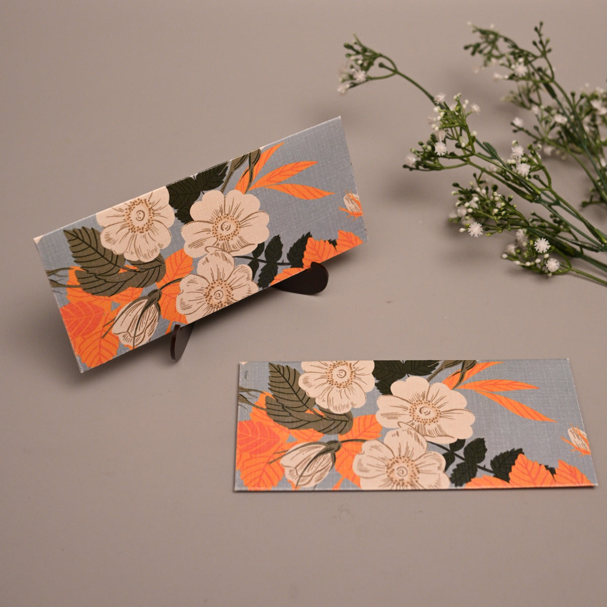 Sagun Envelope with a floral pattern in orange, beige, and green on a gray background