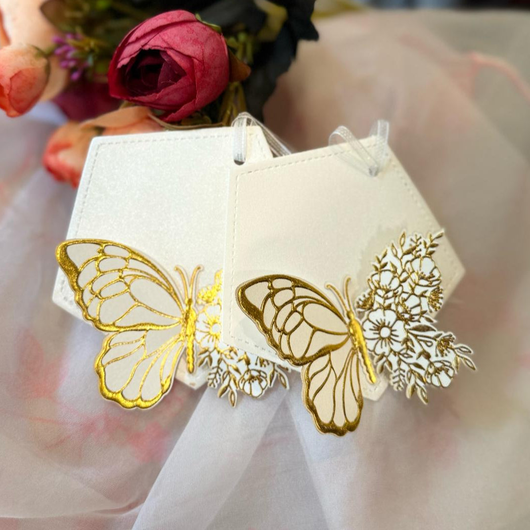 A set of white gift tags with gold foil-embossed butterfly designs, tied with a ribbon.
